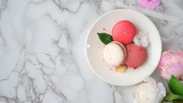 Photo aérienne de macarons pastel colorés sur plaque de céramique blanche avec copie espace, ruban et fleur décorée