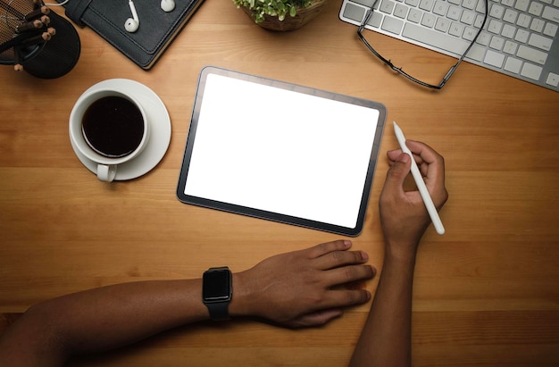Photo aérienne d'une main d'homme tenant un stylet à l'aide d'une tablette numérique sur un bureau en bois