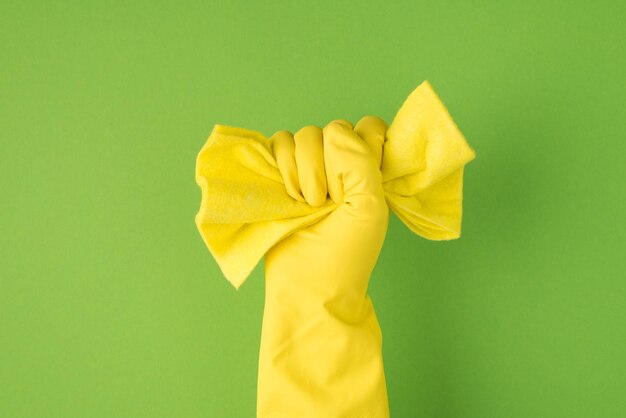 Photo aérienne des mains dans des gants jaunes comprimant un chiffon de nettoyage jaune isolé sur fond vert