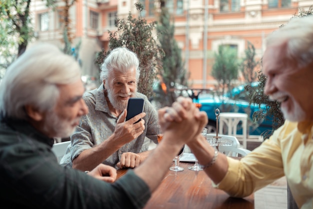 Photo d'amis. Homme aux cheveux gris faisant une photo d'amis faisant un bras de fer alors qu'il était assis à l'extérieur d'un pub