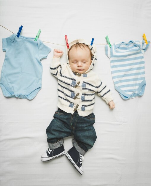 Photo amusante d'un petit garçon en jeans accroché au cordon à côté du séchage des vêtements