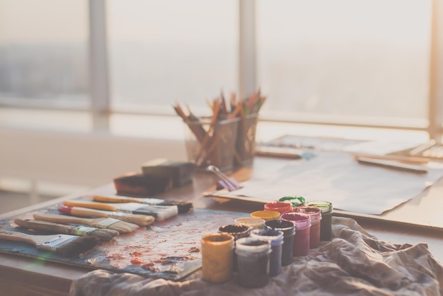 Photo d'angle de la palette avec des peintures à l'huile mixtes, des crayons de gouache et des pinceaux dans un studio d'art