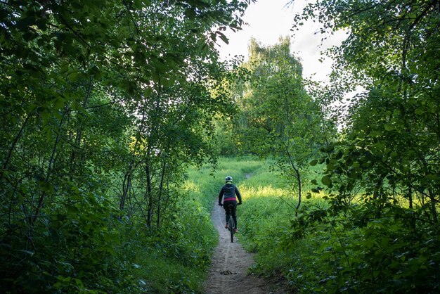 Photo de l'arrière d'une femme cycliste portant un casque à cheval le long de la route dans les bois