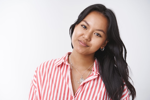 Photo authentique d'une jeune étudiante asiatique séduisante inclinant la tête et souriante devant la caméra envoyant un regard chaleureux comme ayant une bonne humeur et une attitude douce, posant sur fond blanc