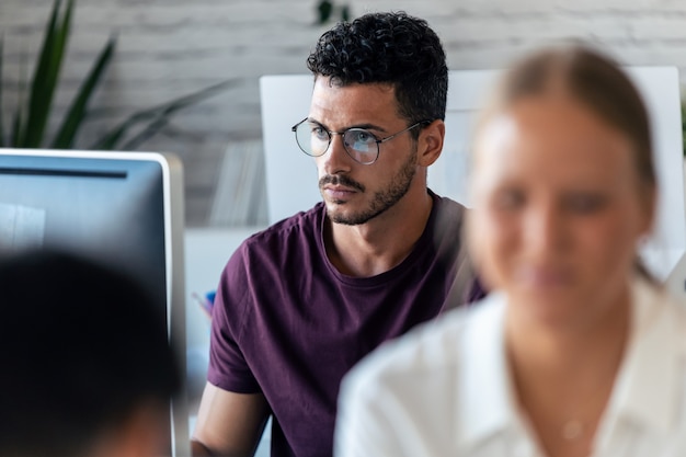 Photo d'un beau jeune entrepreneur utilisant l'ordinateur pendant que ses collègues travaillent ensemble au bureau.