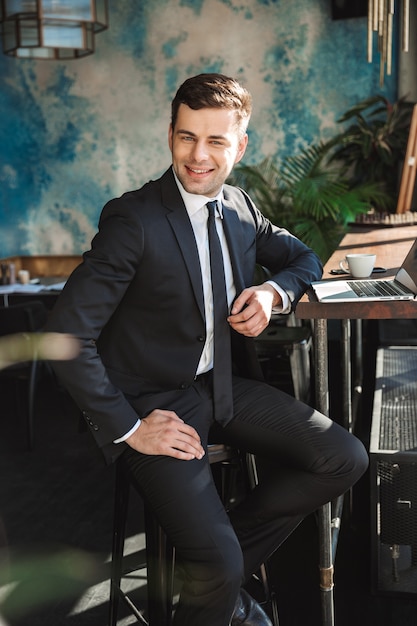 Photo de beau jeune homme d'affaires dans des vêtements formels à l'intérieur dans un café à l'aide d'un ordinateur portable.