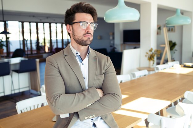 Photo d'un beau jeune homme d'affaires regardant de côté alors qu'il était assis sur une table au bureau.