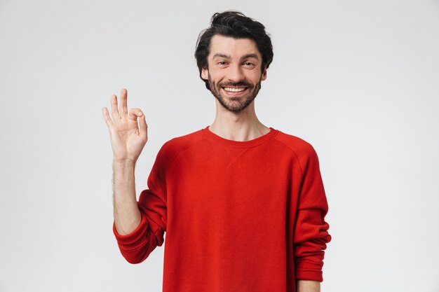 Photo d'un beau jeune homme heureux posant sur un mur blanc fait un geste correct.