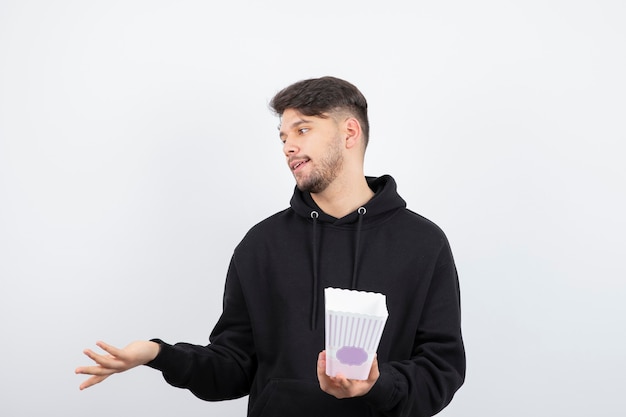 Photo de beau jeune homme regardant des séries télévisées et tenant un seau de pop-corn