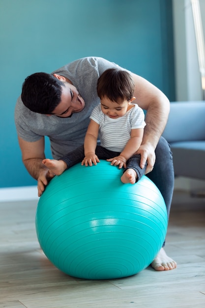 Photo d'un beau jeune père avec son bébé jouant ensemble et s'amusant avec le ballon à la maison.