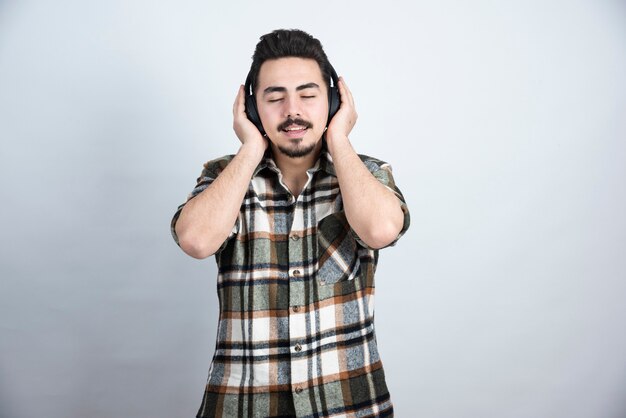 Photo de beau mec dans les écouteurs écoutant une chanson sur un mur blanc.