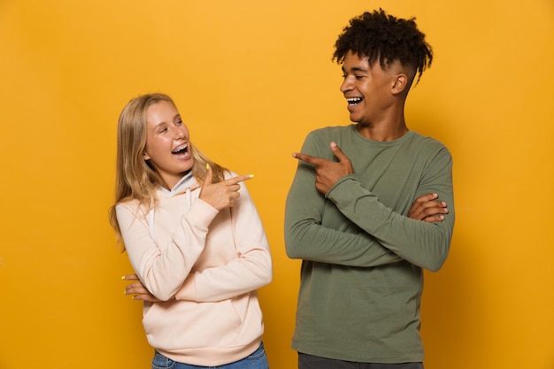 Photo photo de beaux étudiants homme et femme de 16 à 18 ans avec des appareils dentaires riant l'un de l'autre, isolés sur fond jaune