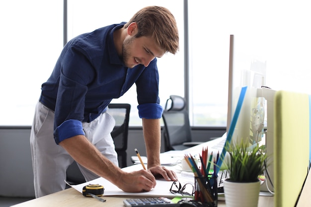 Photo d'un bel architecte masculin travaillant sur un dessin dans son bureau.