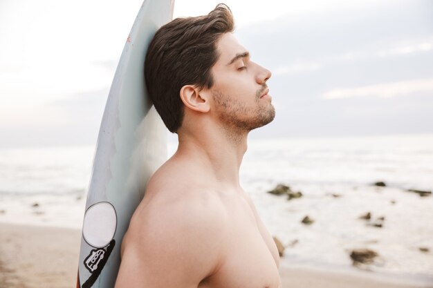 Photo d'un bel homme surfeur avec surf sur une plage à l'extérieur.