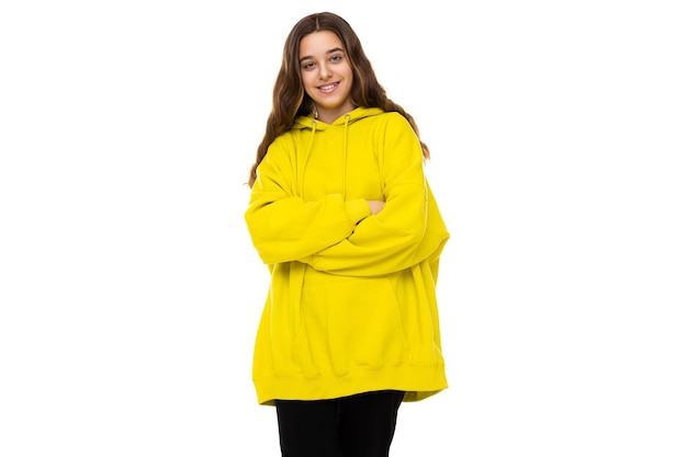 La photo de la belle et adorable adolescente brune en sweat à capuche de sport jaune élégant a croisé les bras