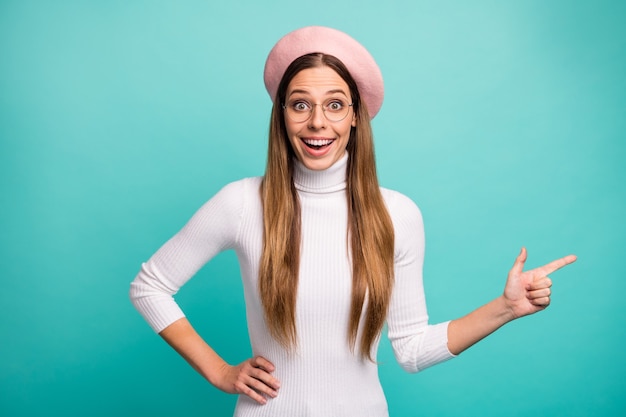 Photo de belle dame gestionnaire choquée côté doigt direct espace vide présentant vente publicité bannière porter des spécifications rose béret casquette col roulé blanc isolé fond de couleur sarcelle