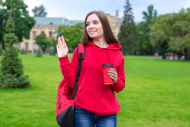 Photo d'une belle dame profitant d'une belle boisson à emporter à emporter thé latte allant aux cours en agitant la paume à quelqu'un