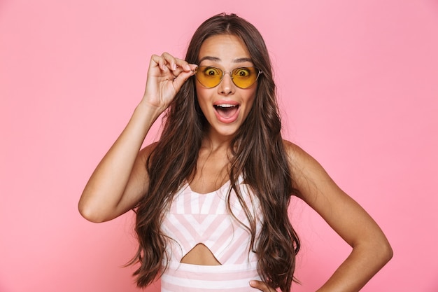 Photo de belle femme 20 ans portant des lunettes de soleil s'amusant et riant, isolé sur mur rose