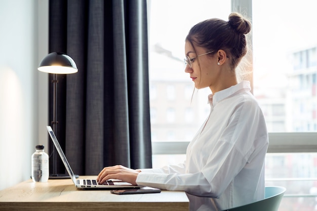 Photo d'une belle femme d'affaires concentrée travaillant avec son ordinateur portable sur le bureau de la chambre d'hôtel.