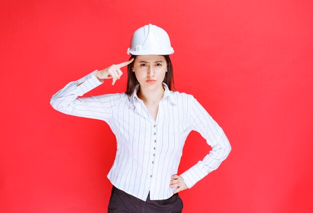 Photo d'une belle femme d'affaires portant un chapeau de sécurité tenant le doigt sur la tempe.