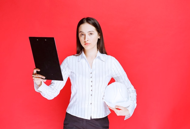 Photo d'une belle femme d'affaires tenant un chapeau de sécurité avec dossier.