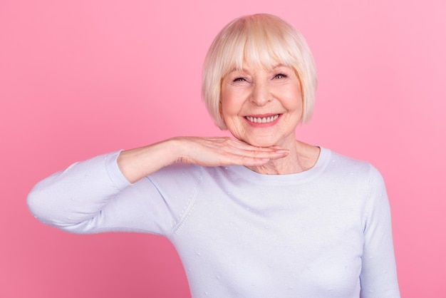 Photo d'une belle femme âgée touchant la main de la procédure de levage en plastique du collagène du menton isolée sur un fond de couleur rose