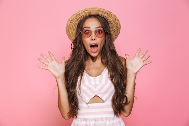 Photo de belle femme des années 20 portant des lunettes de soleil et un chapeau de paille criant, isolé sur un mur rose