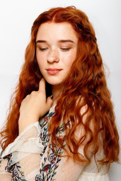 Photo d'une belle femme au gingembre sérieuse, une peau lisse et saine, des cheveux naturels ondulés rouges vêtus d'un pull blanc décontracté regarde les poses de caméra dans l'espace de copie de studio sur le côté droit