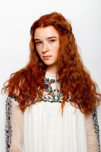 Photo d'une belle femme au gingembre sérieuse avec une peau saine et lisse a des cheveux naturels ondulés rouges vêtus d'un pull blanc décontracté regarde les poses de caméra dans l'espace de copie de studio sur le côté droit