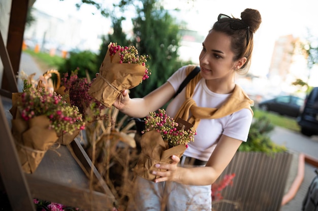 Photo D'une Belle Femme Brune Séduisante Européenne Portant Un T-shirt Blanc élégant Et Un Jean Bleu Choisit Des Fleurs Comme Cadeau Dans Une Boutique De Jardin De Rue De La Ville