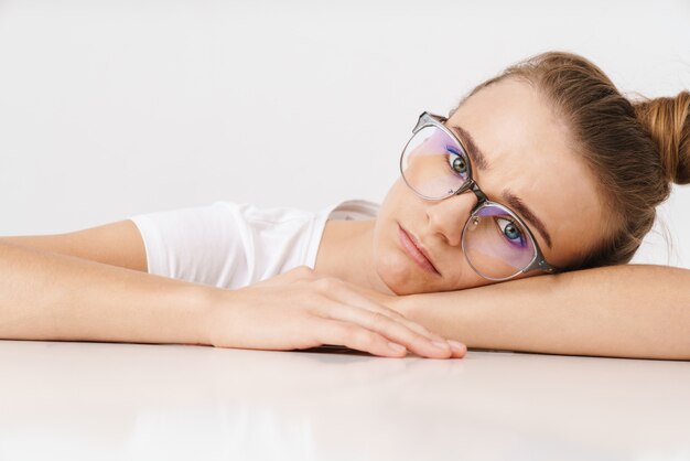 Photo d'une belle femme malheureuse à lunettes regardant la caméra tout en s'appuyant sur la table