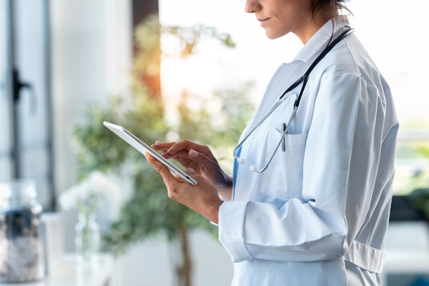 Photo d'une belle femme médecin utilisant sa tablette numérique en se tenant debout lors de la consultation.