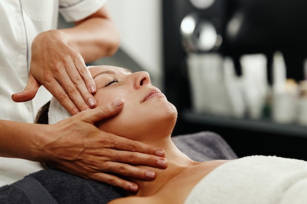 Photo d'une belle femme mûre profitant d'un massage du visage au salon de beauté.