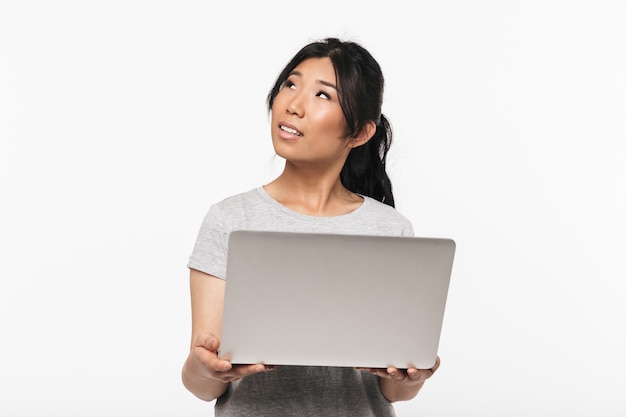 Photo d'une belle jeune femme asiatique joyeuse posant isolée sur un mur blanc à l'aide d'un ordinateur portable.