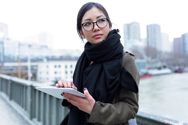Photo d'une belle jeune femme asiatique utilisant sa tablette numérique devant la Seine à Paris.