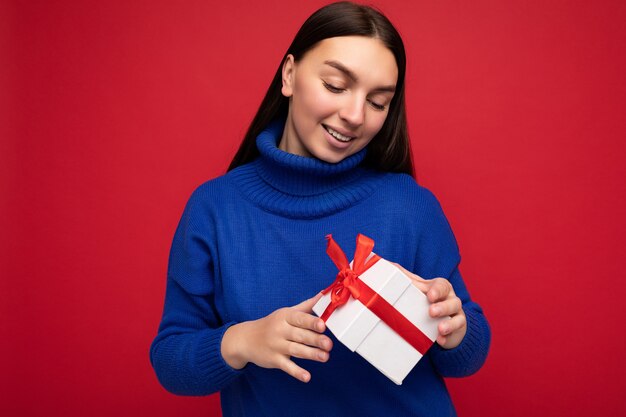 Photo de belle jeune femme brune souriante positive isolée sur mur rouge portant