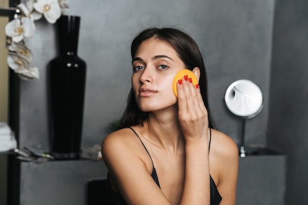 Photo de belle jeune femme dans la salle de bain prendre soin de sa peau avec des produits cosmétiques nettoyer son visage.