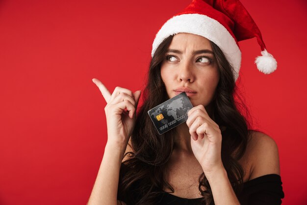 Photo d'une belle jeune femme debout isolée sur un mur rouge tenant une carte de crédit.
