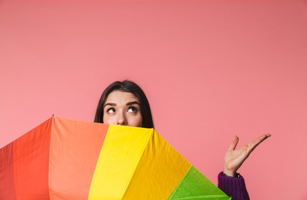 Photo d'une belle jeune femme émotionnelle posant isolée sur un espace rose tenant un parapluie arc-en-ciel montrant fond.