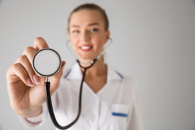 Photo d'une belle jeune femme médecin cosmétologue isolé sur un mur gris tenant un stéthoscope.