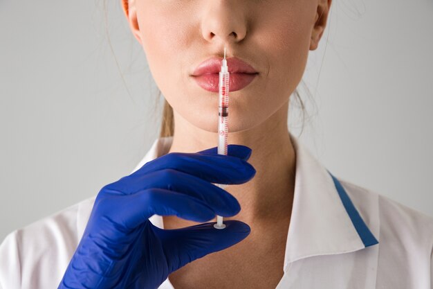 Photo d'une belle jeune femme médecin cosmétologue isolée sur mur gris tenant la seringue d'injection.