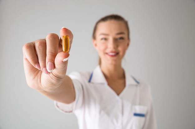 Photo d'une belle jeune femme médecin cosmétologue isolée sur mur gris tenant la vitamine pilule