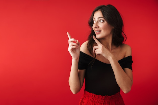 Photo d'une belle jeune femme mignonne debout isolée sur un mur rouge pointant.