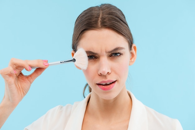 Photo de la belle jeune femme posant isolé tenant des pinceaux de maquillage.