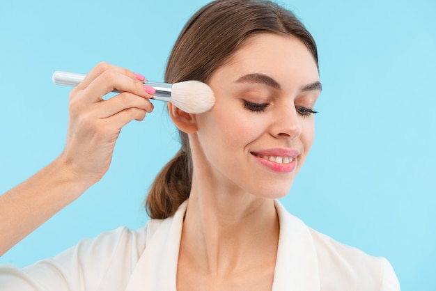 Photo de la belle jeune femme posant isolé tenant des pinceaux de maquillage.