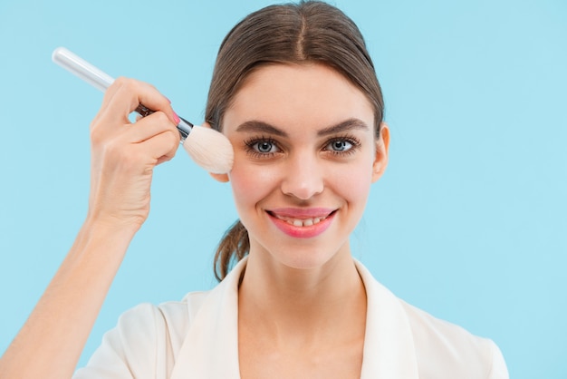 Photo de la belle jeune femme posant isolé tenant des pinceaux de maquillage.