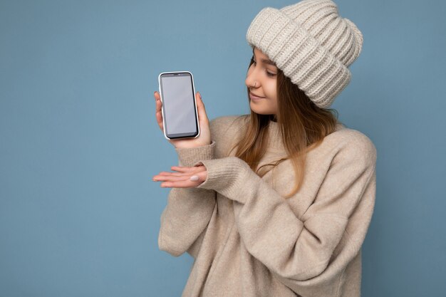 Photo de la belle jeune femme positive à la recherche d'un pull beige élégant et tricoté beige