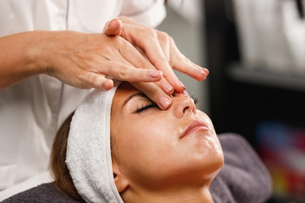 Photo d'une belle jeune femme profitant d'un massage du visage au salon de beauté.