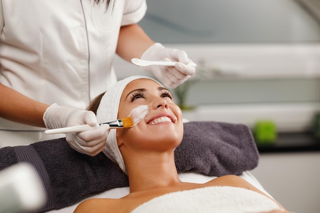 Photo d'une belle jeune femme recevant un masque facial au salon de beauté.