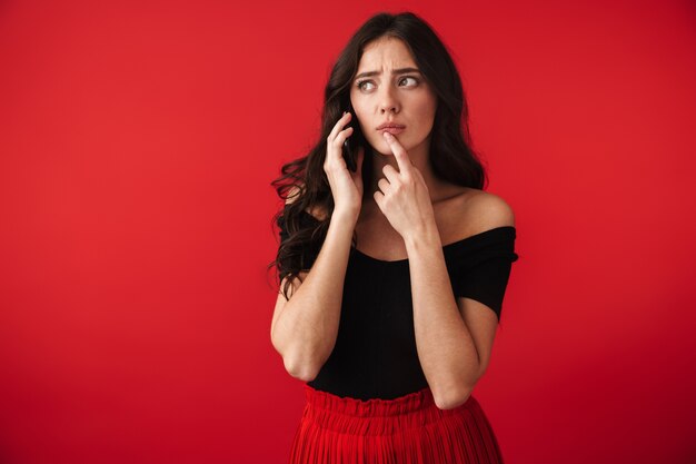 Photo d'une belle jeune femme sérieuse debout isolée sur un mur rouge parlant par téléphone mobile.